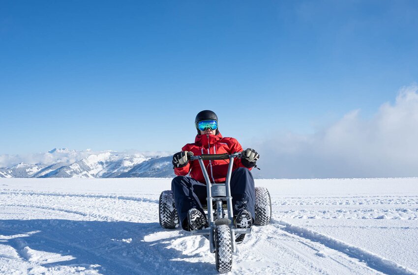 Person mit Helm und roter Jacke fährt Schneekart auf Schnee, Berge im Hintergrund unter blauem Himmel. | © Dorfgasteiner Bergbahnen AG