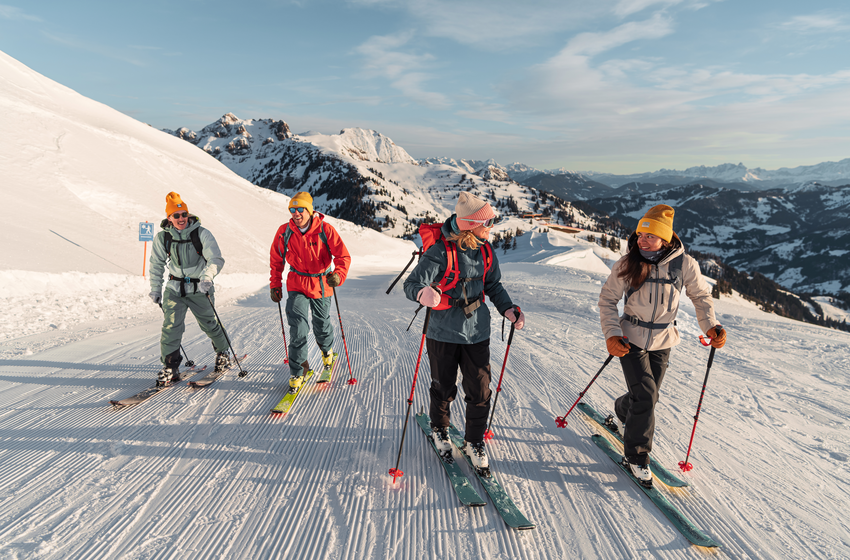 Four ski tourers ascend a groomed slope in sunshine, surrounded by snow-covered Alpine mountains | © Dorfgasteiner Bergbahnen AG