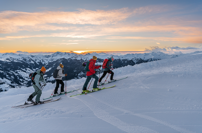 Vier Skitourengeher steigen in Reihe eine verschneite Piste bei Sonnenuntergang in den Alpen hinauf | © Dorfgasteiner Bergbahnen AG