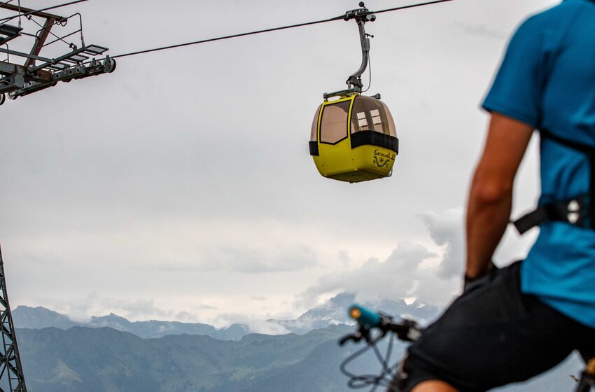Cyclist with helmet looks at yellow Großarl gondola with cloudy sky and alpine mountain panorama in the background | © Grossarler Bergbahnen GmbH & Co KG