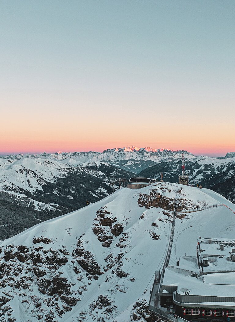 Panorama of snow-covered Stubnerkogel at sunrise with cable car station and alpine mountain view. | © Gasteiner Bergbahnen AG