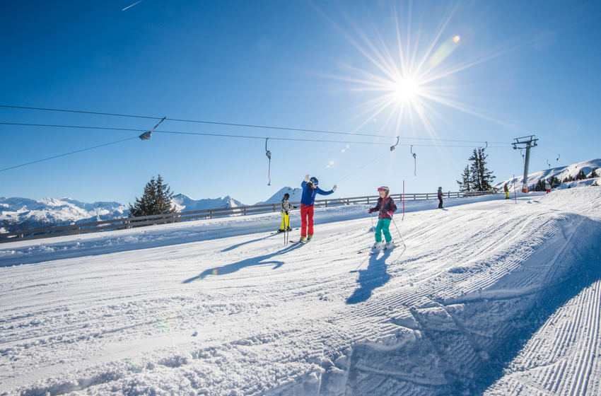 Children and adults skiing in sunshine on a wide slope with drag lift in the background. | © Tourismusverband Großarltal