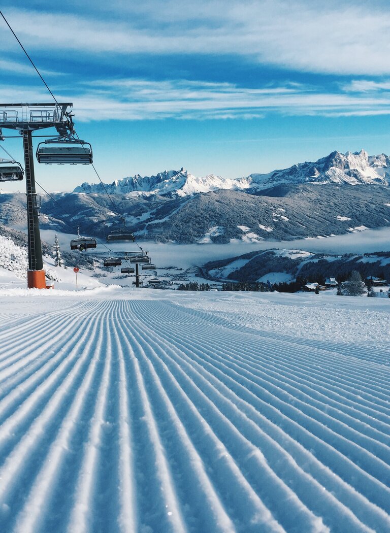 Chairlift above freshly groomed slope in Ski amadé | © Ski amadé GmbH Chairlift above freshly groomed slope with snowy mountain and valley view. | © Ski amadé GmbH