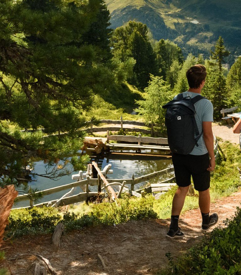 Zwei Wanderer auf Waldweg mit Blick auf kleinen Wasserlauf mit Holzumrandung am Graukogel im Sommer | © Gasteiner Bergbahnen AG
