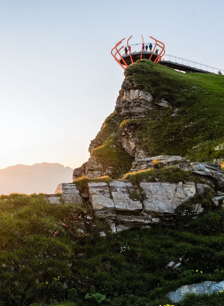 Paar auf Bank im Sonnenuntergang mit Blick auf die Berge, rechts die Plattform Glocknerblick auf grünem Felsen | © Gasteiner Bergbahnen AG